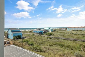A coastal area with buildings, a fenced road, and a beach in the background. - Sandcastle Condominiums Unit 332 (Port Aransas)