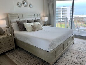 Una camera da letto con un letto grande, un comodino, una lampada e vista sull'oceano da un balcone.