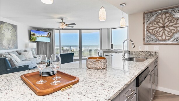 A modern kitchen with a granite countertop, stainless steel appliances, and a large window offering a view of the city. - Sandcastle Condominiums Unit 337 (Port Aransas)