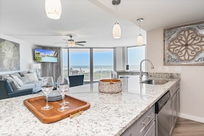 A modern kitchen with a granite countertop, stainless steel appliances, and a large window offering a view of the city. - Sandcastle Condominiums Unit 337 (Port Aransas)