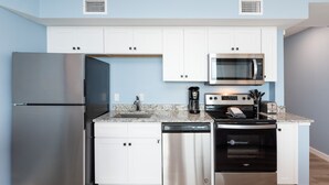 A modern kitchen with white cabinets, stainless steel appliances including a refrigerator, dishwasher, microwave, and oven. - Sandcastle Condominiums Unit 402 (Port Aransas)