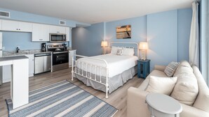 A modern hotel room with a kitchenette, a bed with two bedside tables, a sofa, and a view of the sea. - Sandcastle Condominiums Unit 402 (Port Aransas)