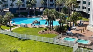 Un hôtel doté d’une piscine centrale, entourée de palmiers et de chaises longues.