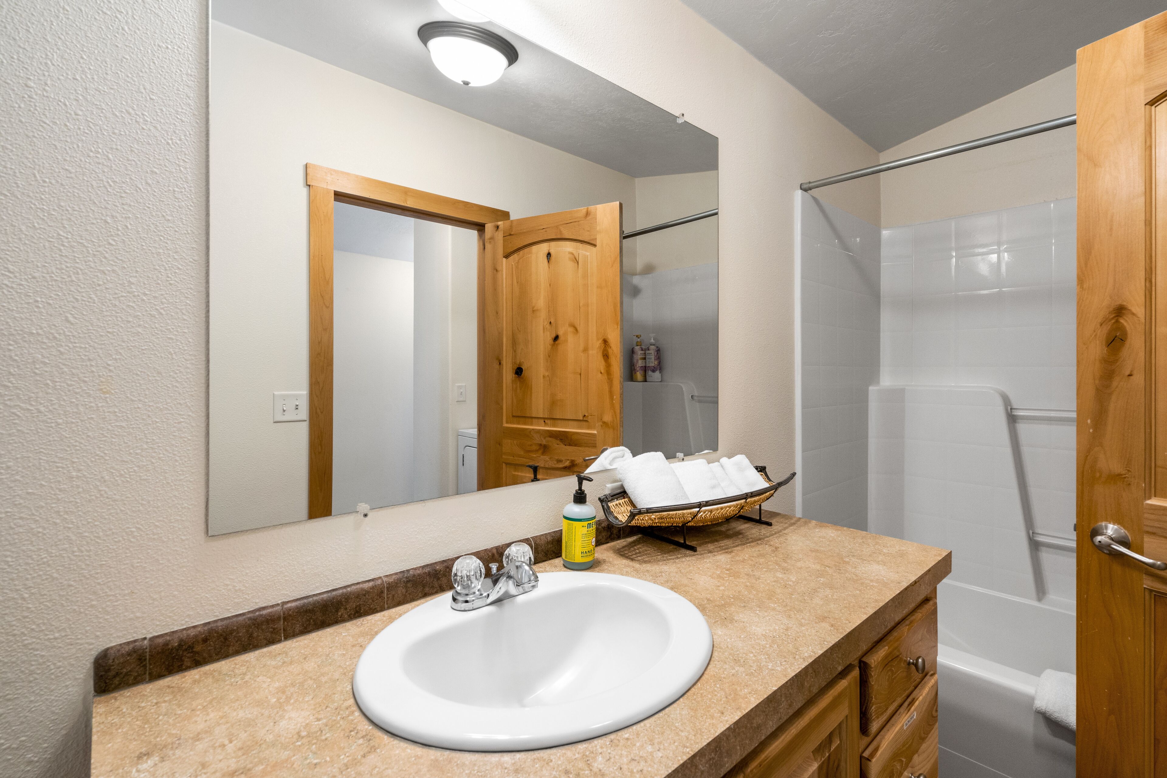 Een badkamer met een witte wastafel, een houten opbergmeubel, een spiegel, een douche en een handdoekhouder.