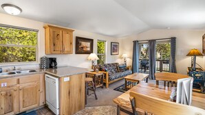Cocina compacta con armarios de madera, lavavajillas y comedor con mesa y sillas de madera.