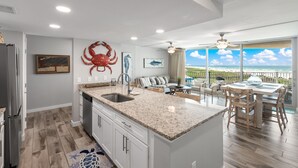 A modern kitchen with a large island, a dining area with a view, and a living space with a large window overlooking the ocean. - Sandcastle Condominiums Unit 404 (Port Aransas)