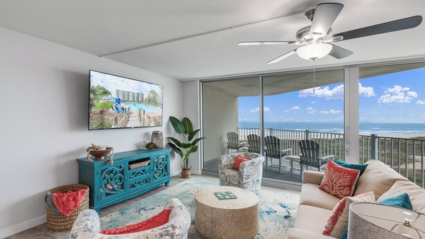 Een ruim balkon met uitzicht op de oceaan, een plafondventilator en een aan de muur bevestigde televisie.