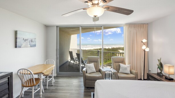 A hotel room with a balcony, a ceiling fan, a dining table with chairs, and a bed. - Sandcastle Condominiums Unit 407 (Port Aransas)