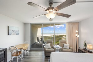 A hotel room with a balcony, a ceiling fan, a dining table with chairs, and a bed. - Sandcastle Condominiums Unit 407 (Port Aransas)