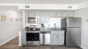 A modern kitchen with grey cabinets, stainless steel appliances, and a wooden floor. - Sandcastle Condominiums Unit 407 (Port Aransas)