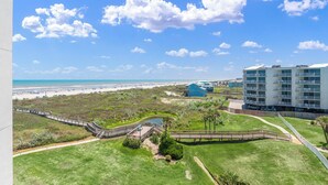 A coastal hotel with a view of the beach, a boardwalk, and a large building with multiple balconies. - Sandcastle Condominiums Unit 407 (Port Aransas)