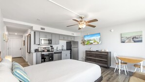 A modern bedroom with a large bed, a desk, and a kitchenette. - Sandcastle Condominiums Unit 407 (Port Aransas)