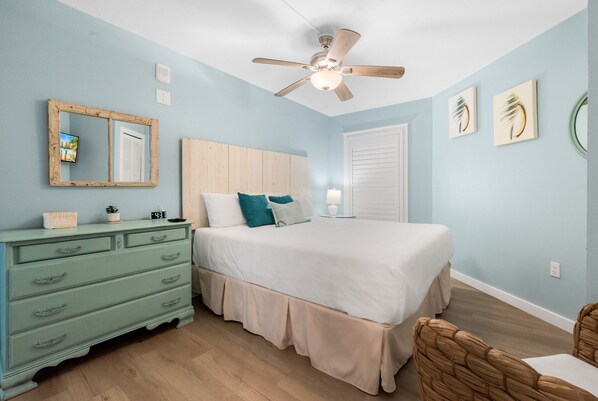 A bedroom with a bed, a dresser, a ceiling fan, and a wall-mounted mirror. - Sandcastle Condominiums Unit 409 (Port Aransas)