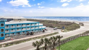 A coastal hotel with multiple balconies, a parking lot, and a view of the beach and ocean. - Sandcastle Condominiums Unit 410 (Port Aransas)