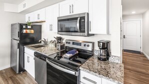 A modern kitchen with stainless steel appliances, white cabinetry, and a granite countertop. - Sandcastle Condominiums Unit 410 (Port Aransas)