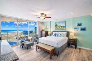 A bedroom with a large bed, a ceiling fan, a view of the ocean, and a balcony with outdoor furniture.