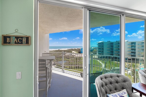 A balcony with a view of the beach, a chair with a pillow, and a sign that reads "BEACH".