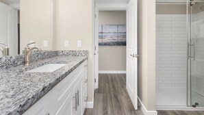 A modern bathroom with a granite countertop sink, white cabinets, and a glass shower enclosure. - Sandcastle Condominiums Unit 415 (Port Aransas)