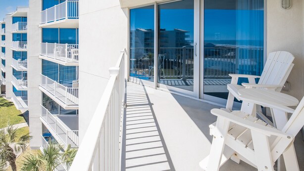 A balcony with white chairs, a glass door, and a view of the ocean. - Sandcastle Condominiums Unit 415 (Port Aransas)