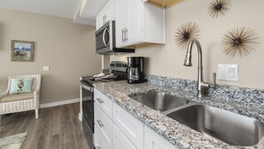 A modern kitchen with white cabinets, granite countertops, stainless steel sinks, and a built-in oven. - Sandcastle Condominiums Unit 415 (Port Aransas)