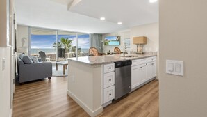 A modern kitchen with a dishwasher, a dining area with a view, and a living room with a sofa. - Sandcastle Condominiums Unit 420 (Port Aransas)