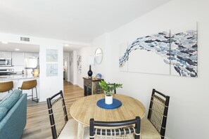 Uma área de refeições com uma mesa redonda, cadeiras e um jogo americano azul. Há uma planta sobre a mesa e obras de arte nas paredes.