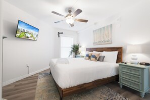 Quarto com cama, ventilador de teto, televisão, pintura e mesa de cabeceira.