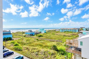 A coastal view with beachfront buildings, a grassy area, and a clear sky. - Sandcastle Condominiums Unit 428 (Port Aransas)