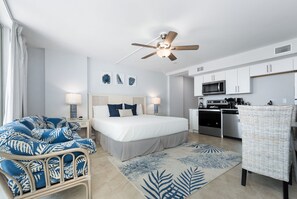 A bedroom with a bed, bedside lamps, a ceiling fan, and a view of a kitchen.