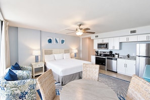 Quarto de hotel com cama, mesa de jantar, área de cozinha e ventoinha no teto.