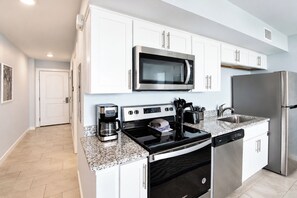 A modern kitchen with white cabinets, stainless steel appliances, a coffee maker, and a dishwasher. - Sandcastle Condominiums Unit 428 (Port Aransas)