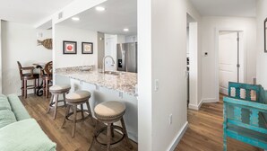 A modern kitchen with a central island, bar stools, and a dining area with chairs. - Sandcastle Condominiums Unit 430 (Port Aransas)
