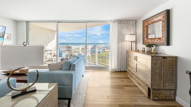 A modern living room with a large sliding glass door leading to a balcony with a view of the sea. - Sandcastle Condominiums Unit 430 (Port Aransas)