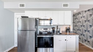 A modern kitchen with stainless steel appliances, white cabinetry, and a patterned backsplash. - Sandcastle Condominiums Unit 502 (Port Aransas)
