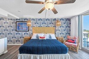 A bedroom with a large bed, a ceiling fan, and a view of the city. - Sandcastle Condominiums Unit 502 (Port Aransas)