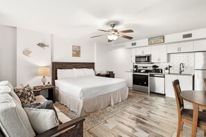A modern hotel room with a large bed, a dining table, a kitchenette, and a ceiling fan. - Sandcastle Condominiums Unit 503 (Port Aransas)
