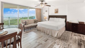 A bedroom with a large bed, a sofa, a dining table, and a view of the ocean. - Sandcastle Condominiums Unit 503 (Port Aransas)