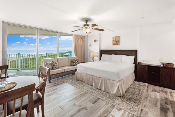 A bedroom with a large bed, a sofa, a dining table, and a view of the ocean. - Sandcastle Condominiums Unit 503 (Port Aransas)