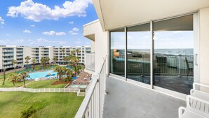 A balcony with a view of a pool and palm trees, overlooking a hotel complex. - Sandcastle Condominiums Unit 503 (Port Aransas)