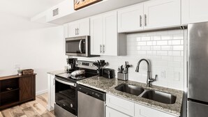 A modern kitchen with white cabinets, stainless steel appliances, a granite countertop, and a double sink. - Sandcastle Condominiums Unit 503 (Port Aransas)