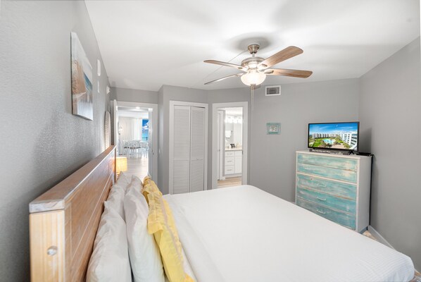 Une chambre à coucher comprenant un lit, un ventilateur de plafond, une commode et un téléviseur.