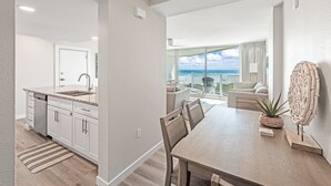 A modern kitchen with a dishwasher, a dining area with a wooden table and chairs, and a balcony with a view of the ocean. - Sandcastle Condominiums Unit 509 (Port Aransas)