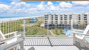 A balcony with white railings overlooking a beach, a pool, and a building with multiple balconies. - Sandcastle Condominiums Unit 509 (Port Aransas)