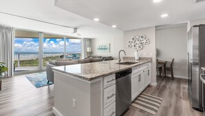 A modern kitchen with a large island, a dining area with a view, and a living space with a sofa and a balcony. - Sandcastle Condominiums Unit 509 (Port Aransas)