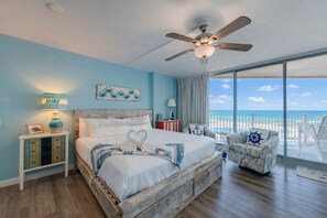 Une chambre avec un lit, une table de chevet, une chaise, un ventilateur de plafond et une vue sur la plage.