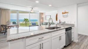 A modern kitchen with a large island, a dishwasher, and a view of the ocean. - Sandcastle Condominiums Unit 518 (Port Aransas)