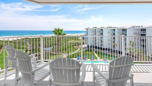 A balcony with white Adirondack chairs overlooking a beach and a pool area. - Sandcastle Condominiums Unit 518 (Port Aransas)