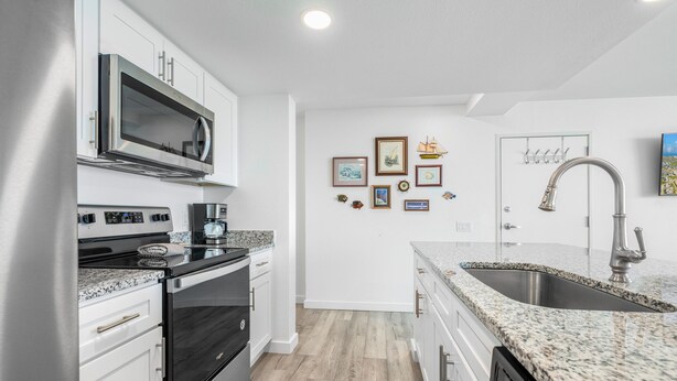 A modern kitchen with stainless steel appliances, granite countertops, and a backsplash. There are framed pictures on the wall and a sink with a modern faucet. - Sandcastle Condominiums Unit 518 (Port Aransas)