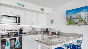 A modern kitchen with white cabinets, a stainless steel microwave, and a granite countertop. - Sandcastle Condominiums Unit 519 (Port Aransas)