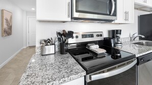 Een moderne keuken met witte kastjes, een roestvrijstalen magnetron, een zwarte kookplaat en een granieten aanrecht.